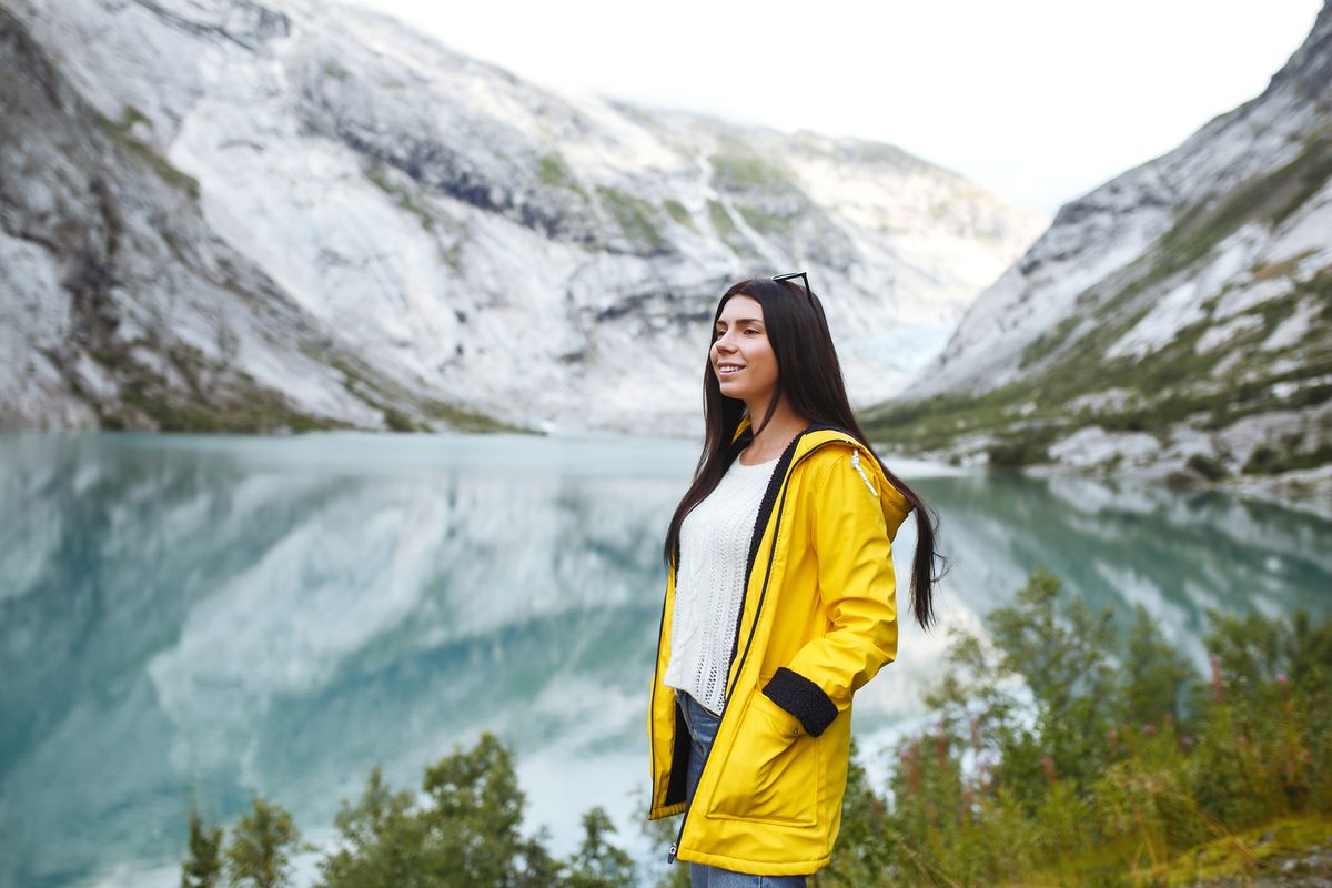 Girl tourist in yellow jacket posing on the lake in Norway. Active woman relaxing in the Norway.
