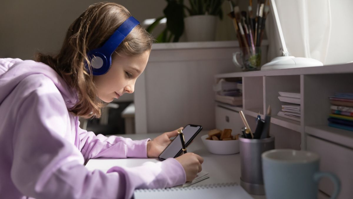 Focused,Teenage,Girl,Wearing,Headphones,Holding,Smartphone,With,Empty,White