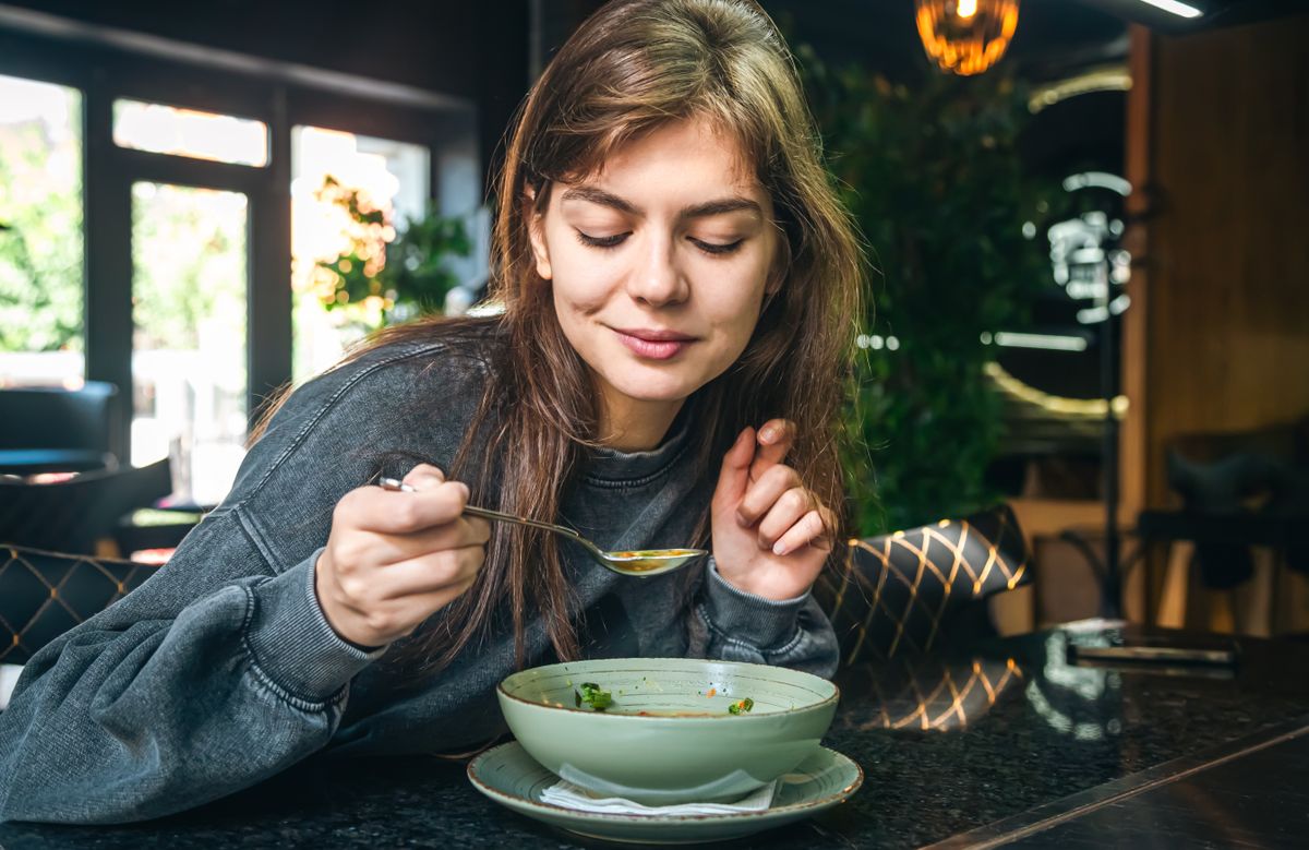 Attractive woman is eating vegetable soup in a cafe.