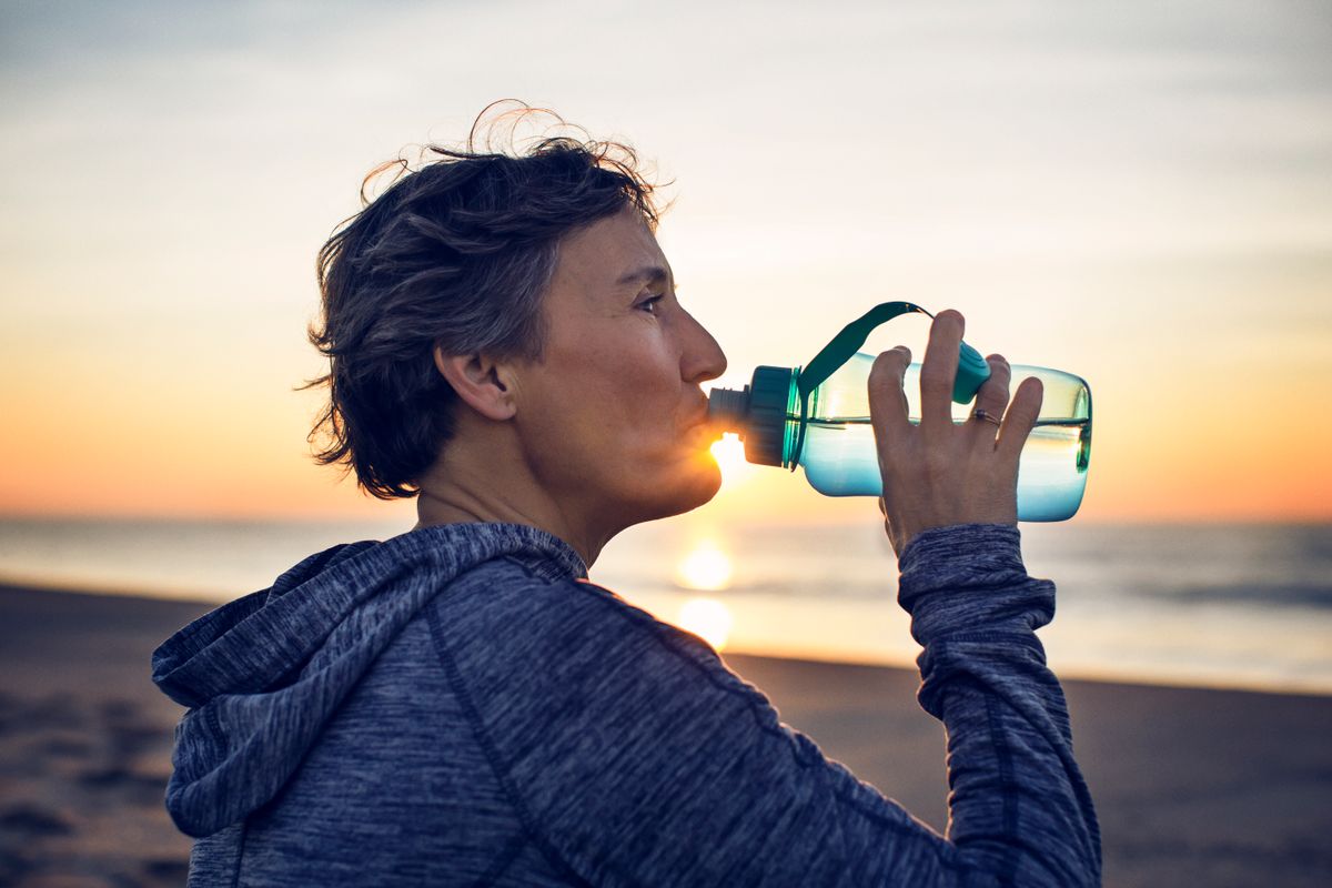 Close-up of woman drinking water at beach against sky
